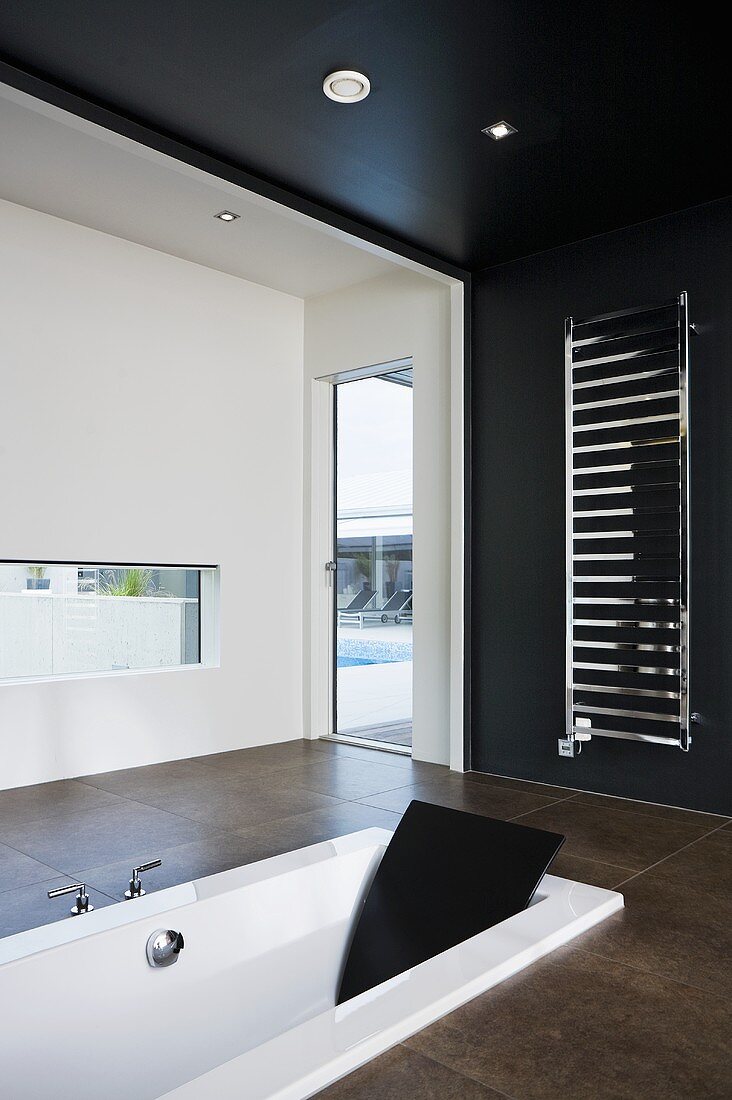 Black and white designer bathroom with sunken bathtub and towel warmer on a black wall