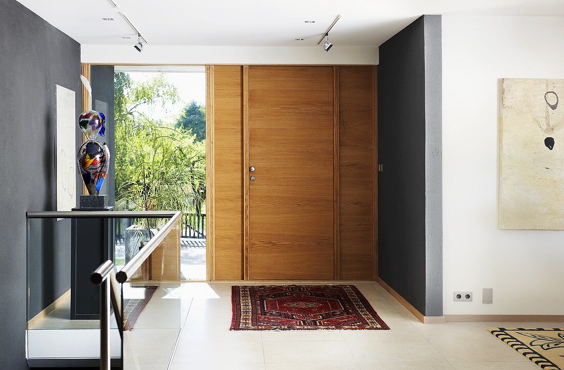 A hallway in a house with a wooden door, a grey wall and a glass balustrade