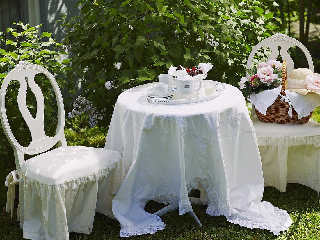 Festlich gedeckter Tisch mit Teeservice und Korb auf Hussenstuhl im Garten