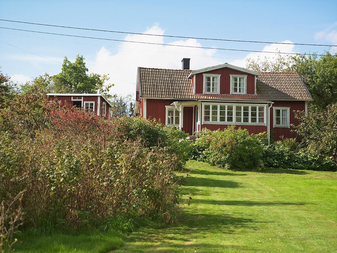 Garten mit rotgestrichenem Holzhaus und weissen Fenster