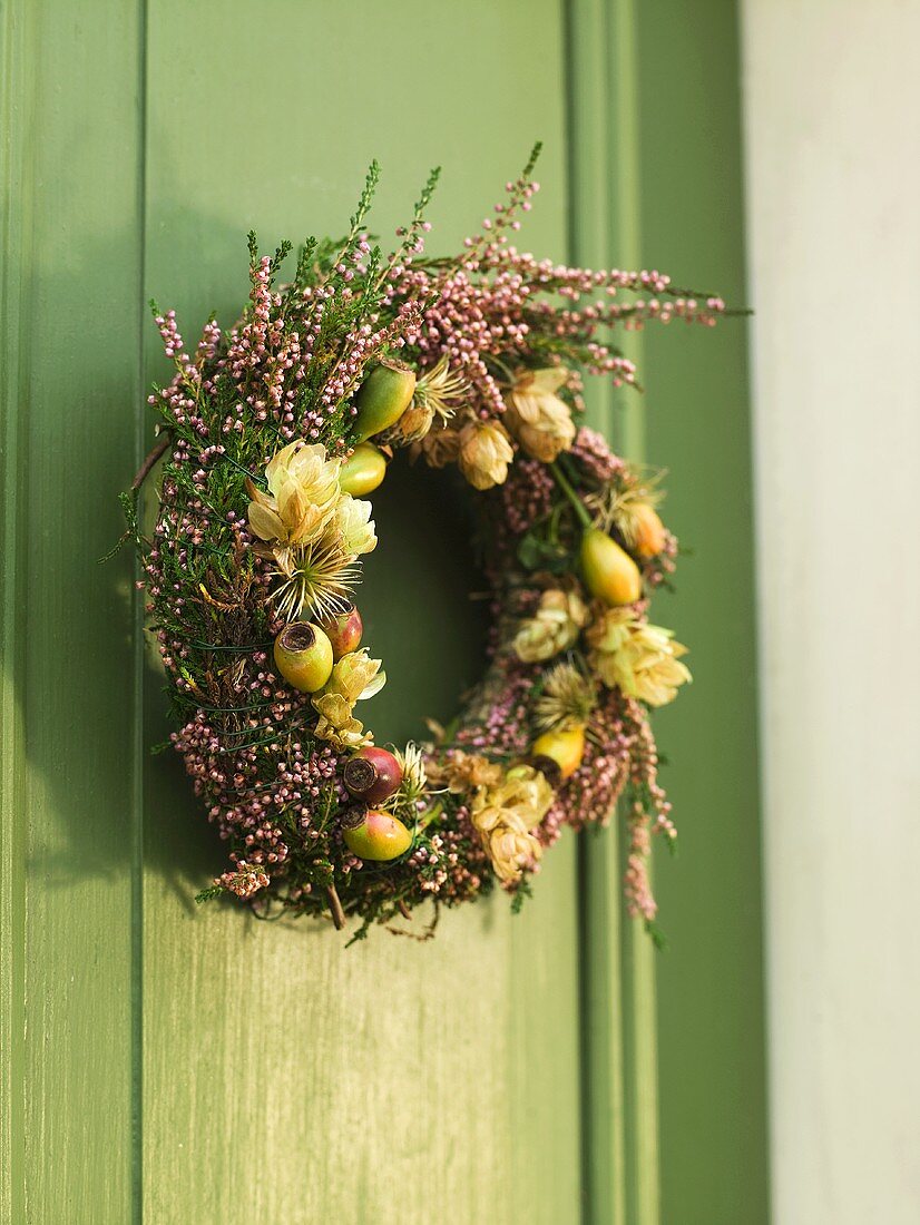 Kranz aus Trockenblumen und Früchten an grüner Holztür