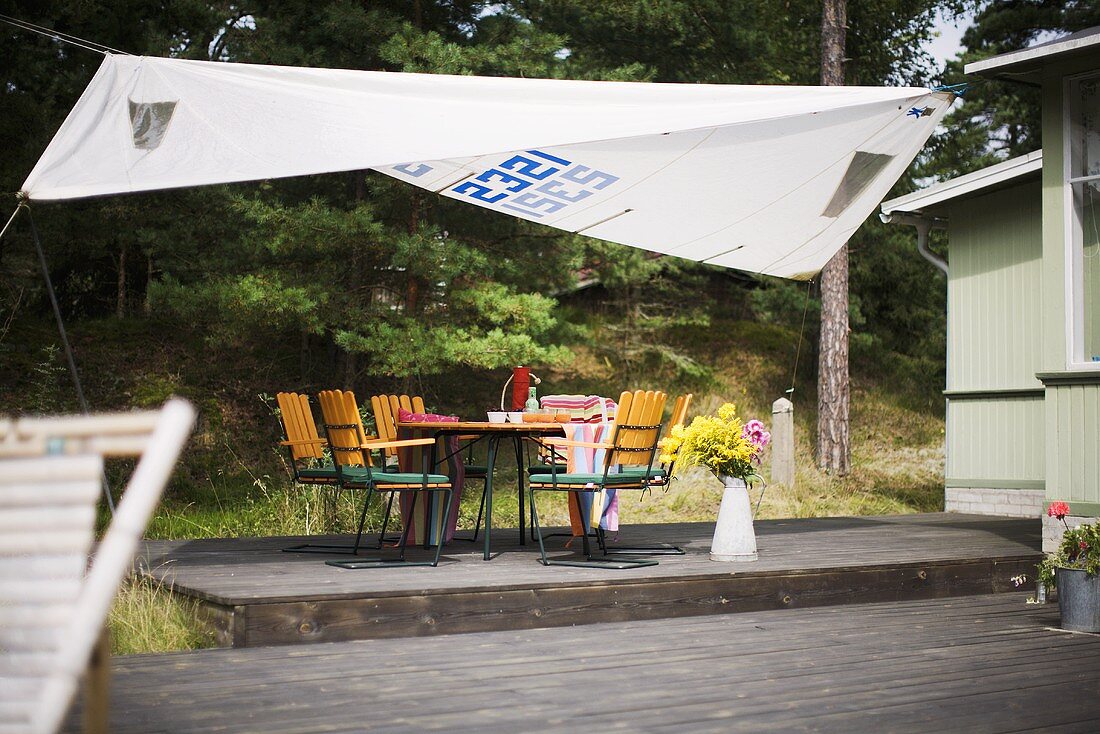 Sonnensegel über Gartentisch mit Stühlen auf Holzterrasse