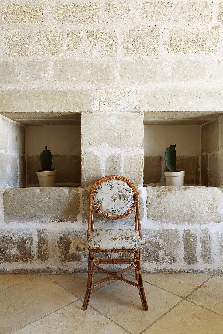 Wall niches with cacti in a stone wall and upholstered rattan chair