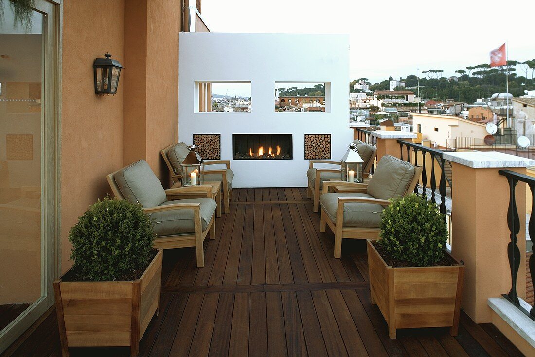 Stimmungsvolles Kaminfeuer auf Dachterrasse mit Holzboden und Sesseln mit grauen Polstern