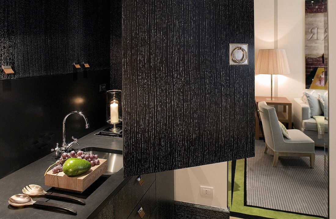 Offenstehende Tür einer schwarzen Schrankküche mit Spüle in Küchenzeile und Blick in Wohnraum