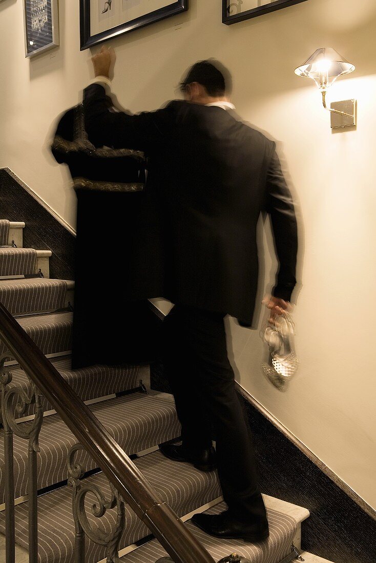 Person with clothes on a hanger in his hand running up stairs