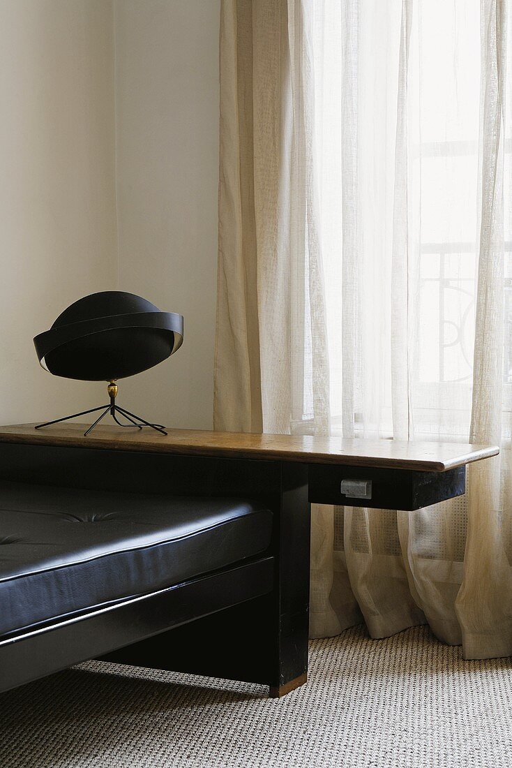 Corner of a room -- black leather couch with a wooden footboard