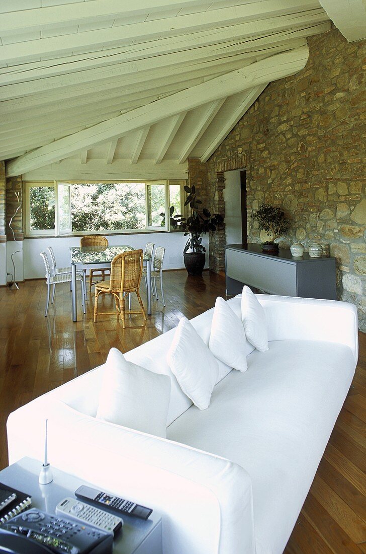 Weisses Sofa unter Holzbalkendecke und Natursteinwand im Wohnraum eines Landhauses