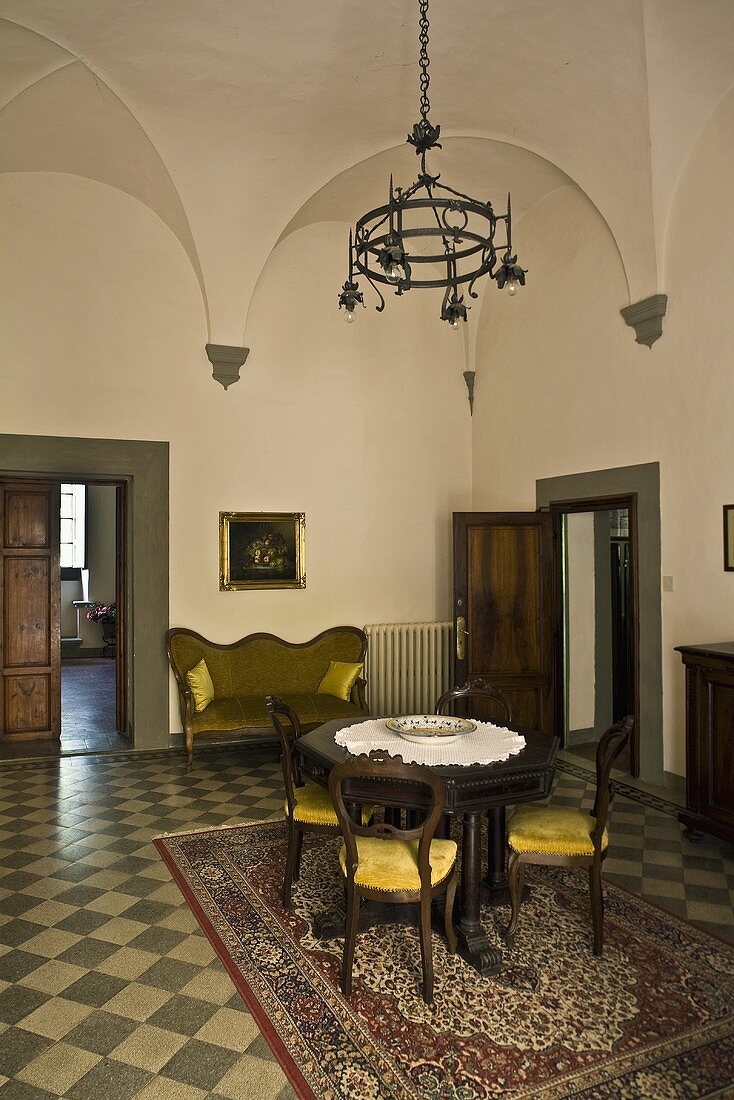 Vaulted ceiling in the salon of a villa with antique furniture on a floor with checkerboard pattern and a view of an open door