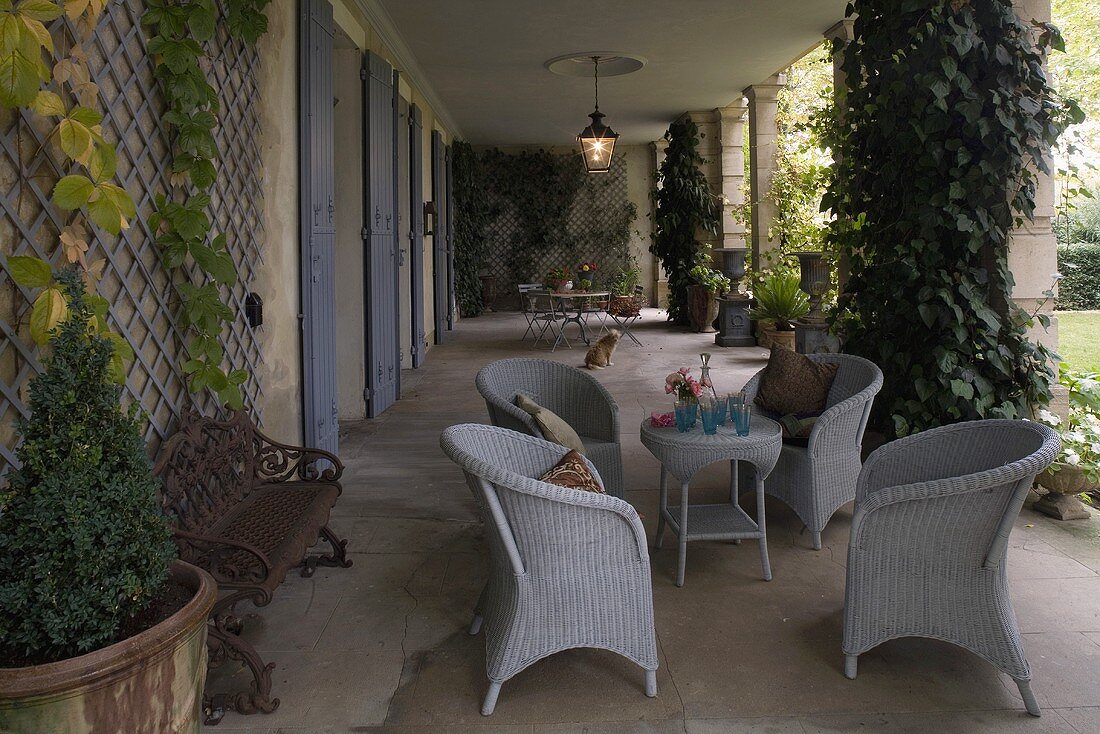 Light gray wicker furniture and planters in the loggia of a villa with a garden view