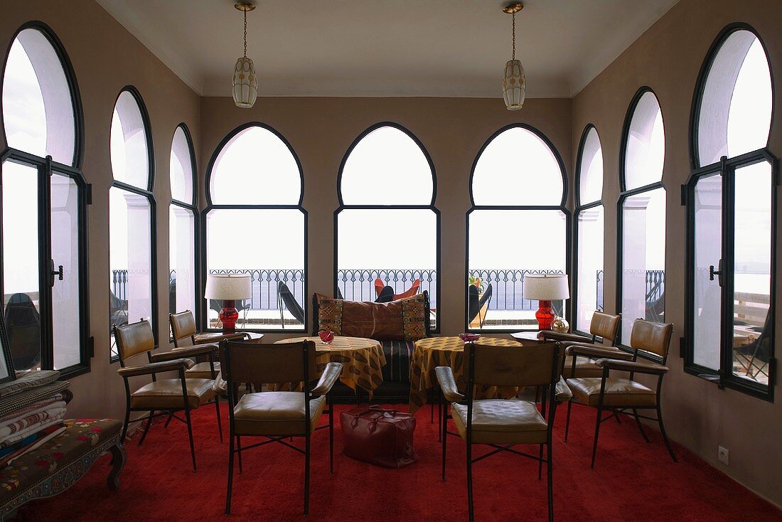 Salon with oriental lancet windows and leather chairs in front of tables on a red carpet