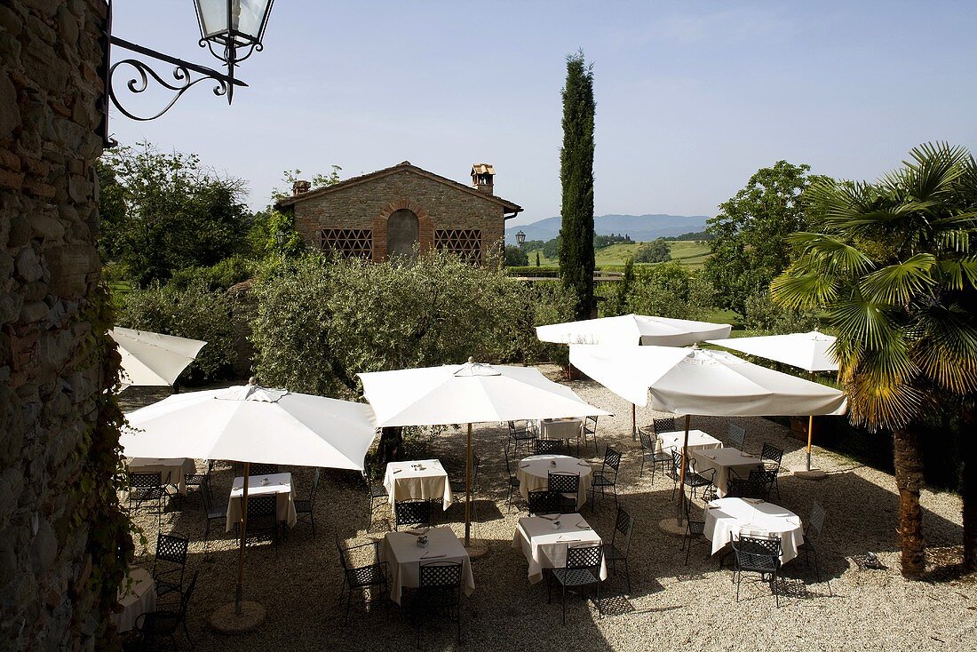 Restaurantterrasse mit Essplätzen unter Sonnenschirm und Blick auf Mediterraner Landschaft