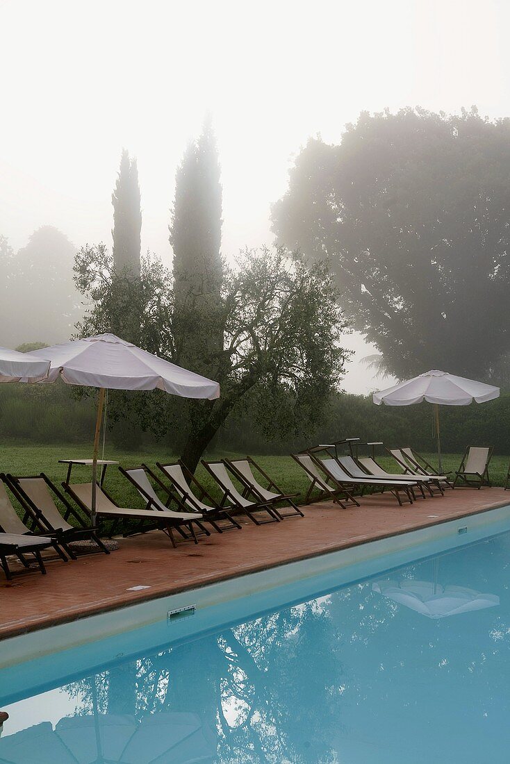 Neblige Morgenstimmung am Pool mit Liegestühlen und Sonnenschirm