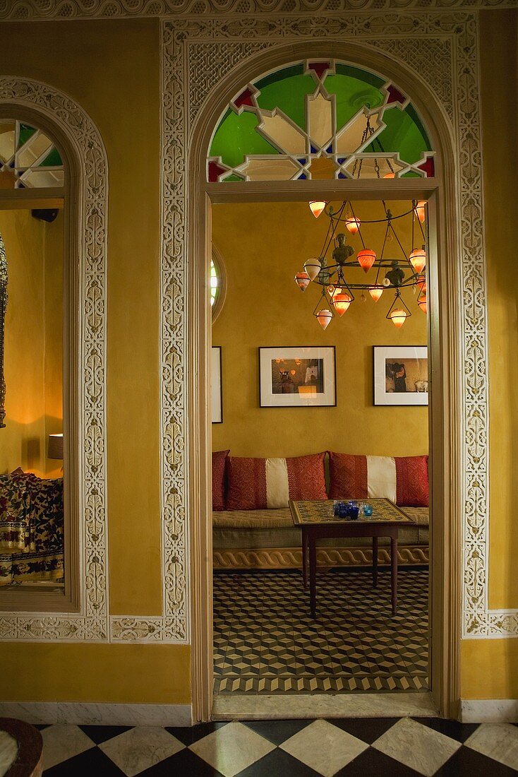 View through a rounded arch into a Moroccan living room with borders on the yellow walls and patterned tile floors