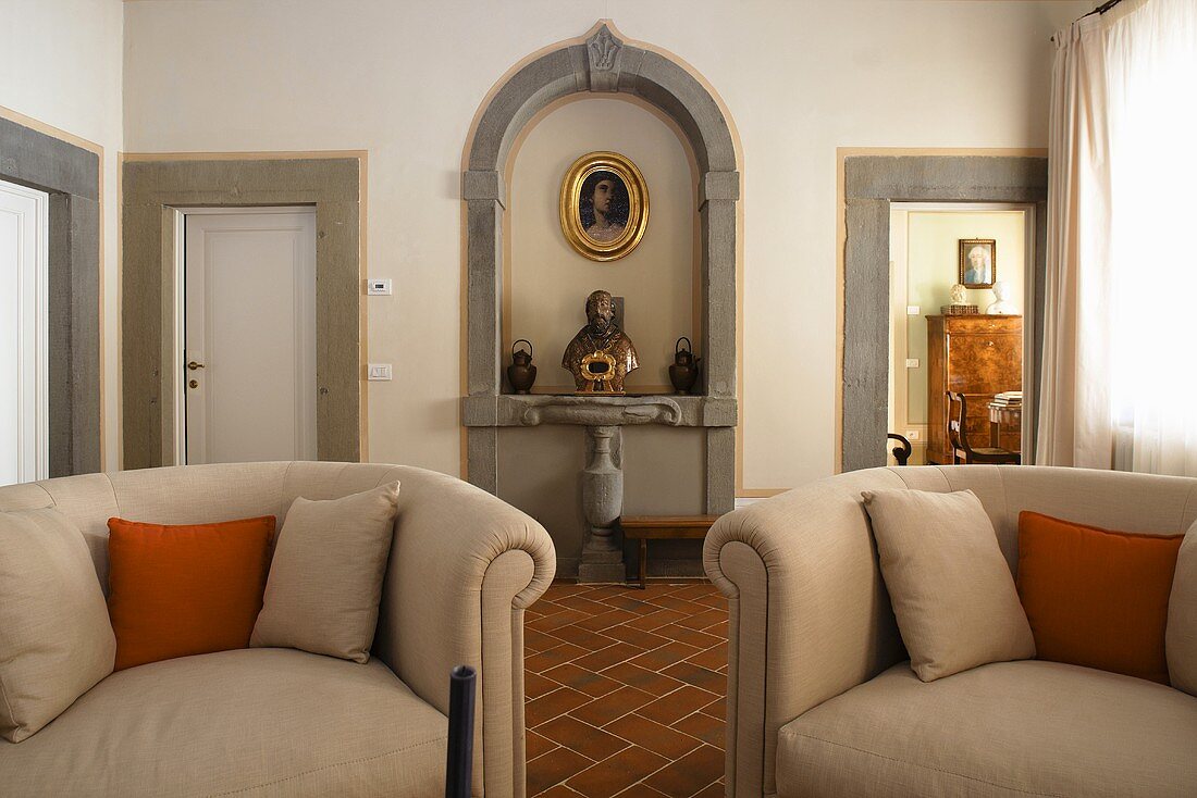 Armchairs upholstered in light gray and busts in a wall niche framed with stone