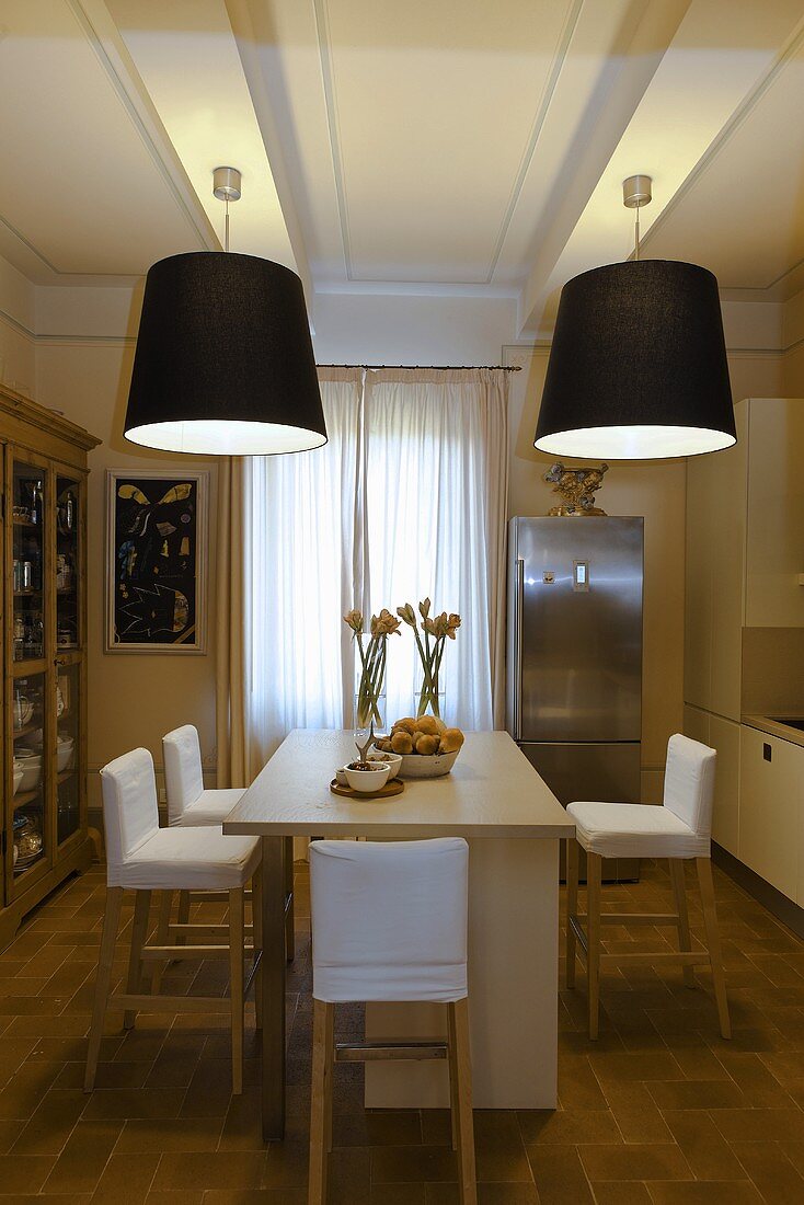 Dining room with black lampshades hanging from the ceiling and a kitchen counter with bar stools