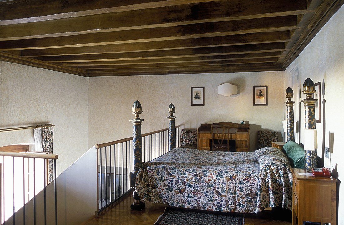 Four poster double bed on a mezzanine under a beam ceiling in a country home