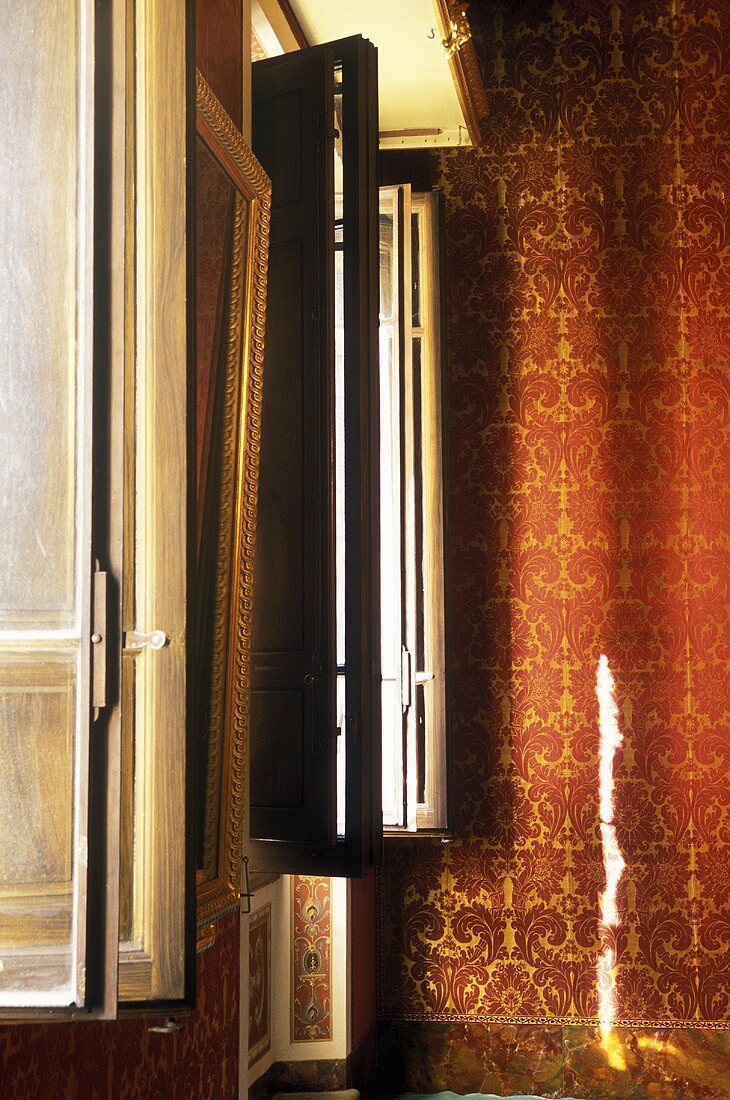 Fenster mit Innenläden und Wand mit rotgoldenem Ornamentmuster