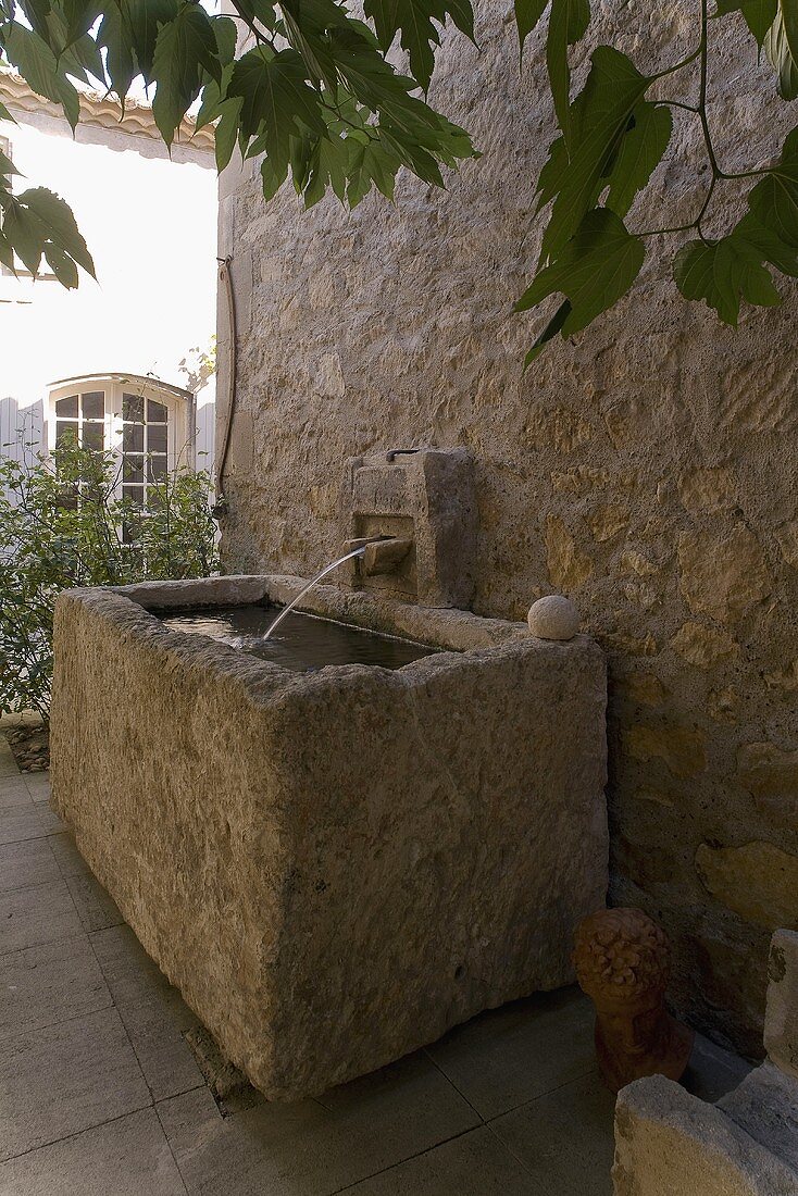 Rustikales Steinbecken mit Wasser vor Natursteinwand und Wasserspeier
