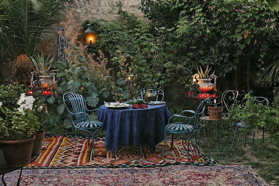 Romantisches Picknick - blaue Gartenmöbel auf orientalischer Decke mit Laterne und Windlichter