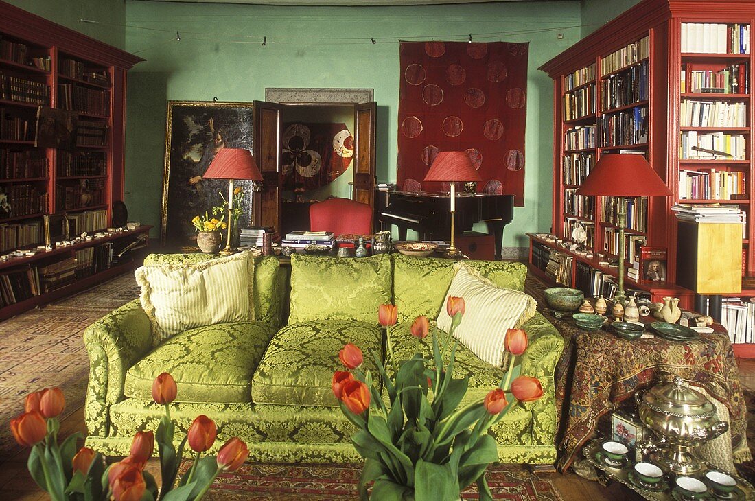 Living room with a green sofa and mahogany bookcases in front of a green wall