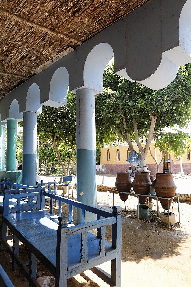 Blue benches under a straw roof with oriental architectural elements and view of clay planters, Egypt
