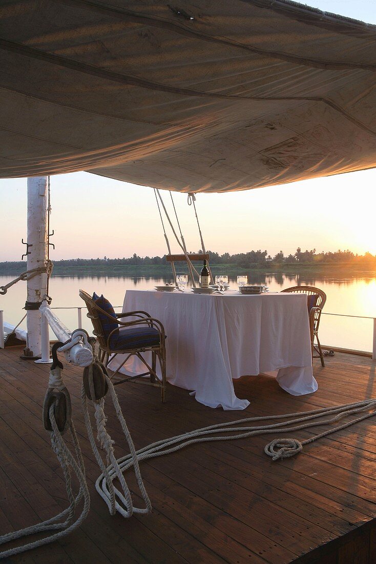 Romantische Abendstimmung am Fluss - gedeckter Tisch für Zwei auf überdachtem Sonnendeck eines Bootes
