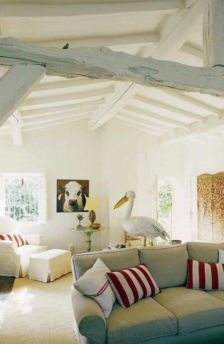Living room with a sofa and red and white cushions in a converted attic with rustic white wood construction ceiling