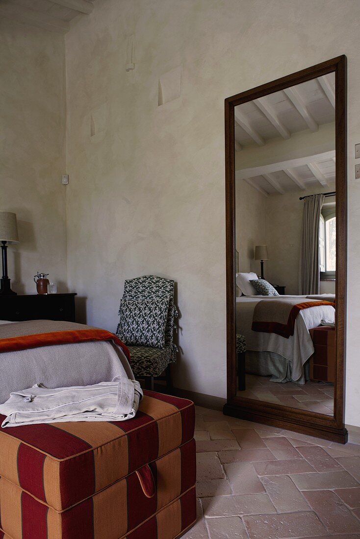 Ländliches Schlafzimmer - gestreifter Polsterwürfel am Bettende und Wandspiegel auf Terrakottaboden