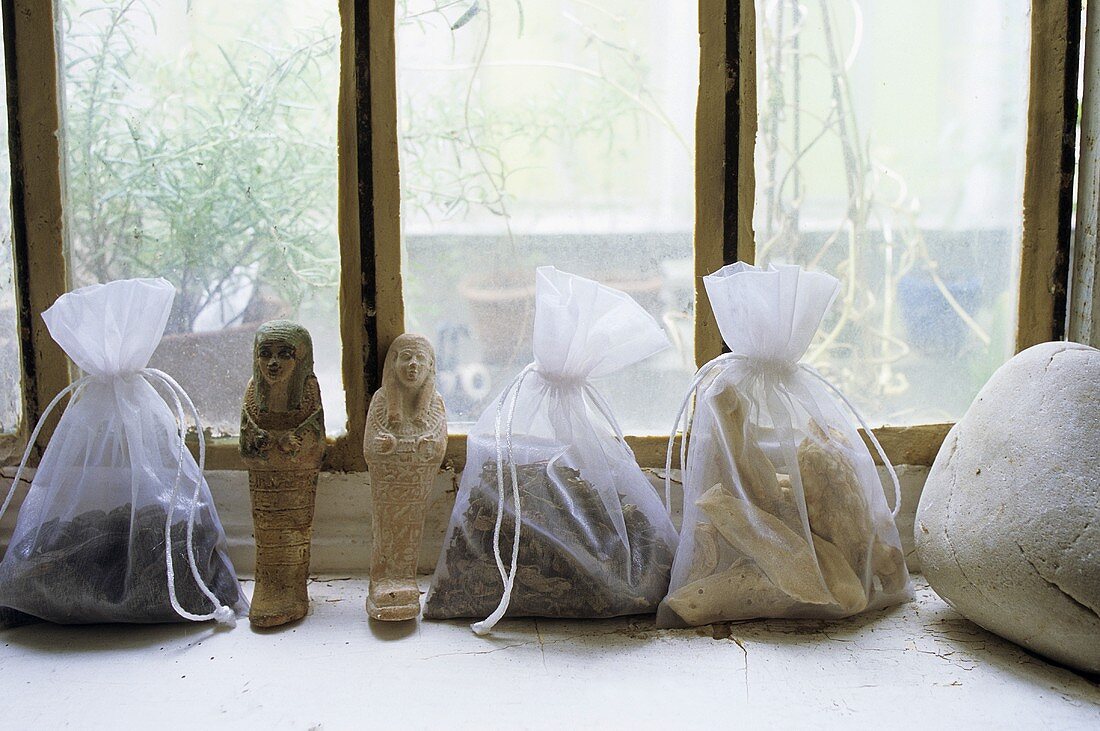 Geschnürte und gefüllte Plastiksäckchen auf Fensterbank und kleine Steinfiguren
