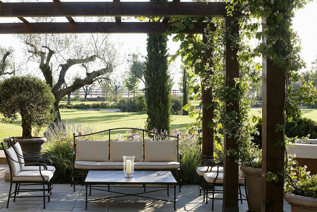 Elegant metal patio furniture upholstered in bright fabric under a pergola with a garden view