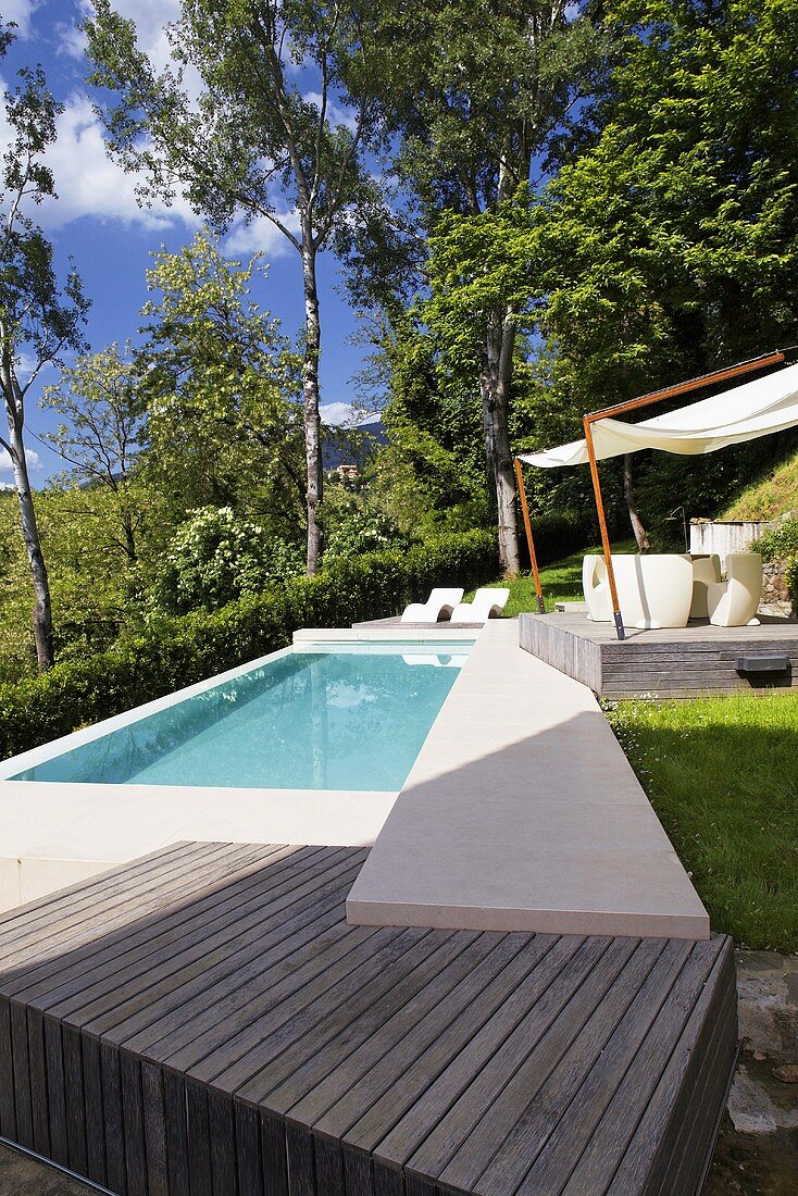 Türkisfarbener Pool im Garten mit Holzpodest und Steg aus Stein