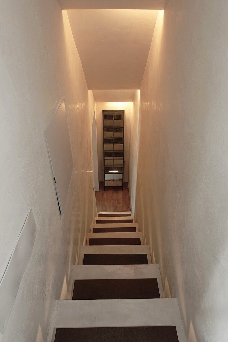 Schmales Treppenhaus mit indirekter Beleuchtung und Blick auf Schrank vor Treppenabgang
