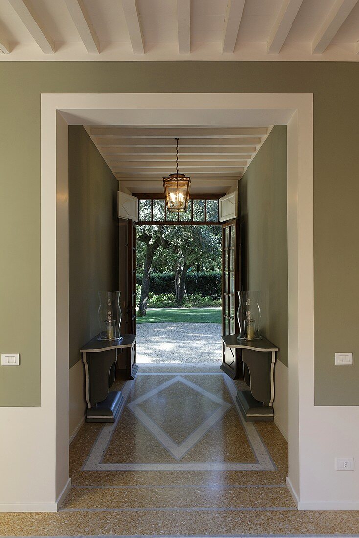 An open hallway in a villa with a terrazzo floor and view of the garden
