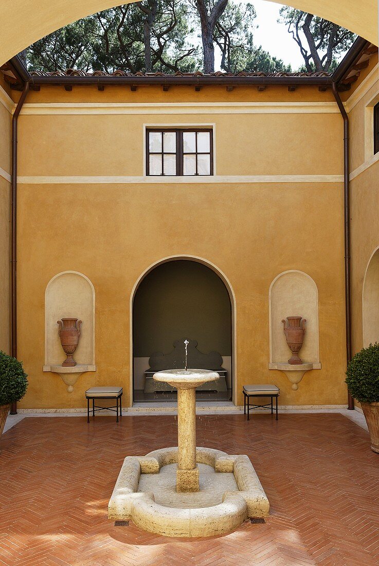 Steinbrunnen im Innenhof einer Mediterraner Villa mit Terrakottaboden und gelber Fassade