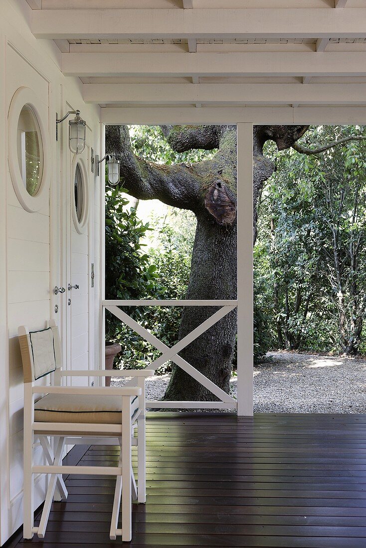 Stuhl auf Holzterrasse mit weißem Geländer und Stütze und Gartenblick