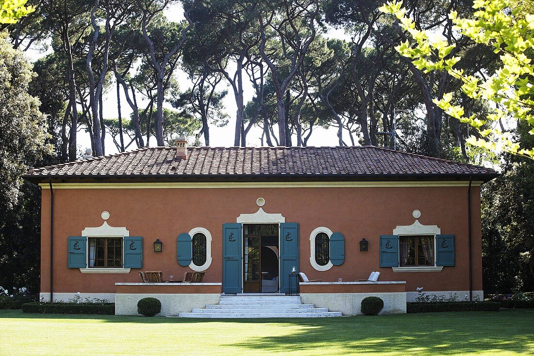 Mediterranean villa with a red brick facade and blue-gray shutters in a garden