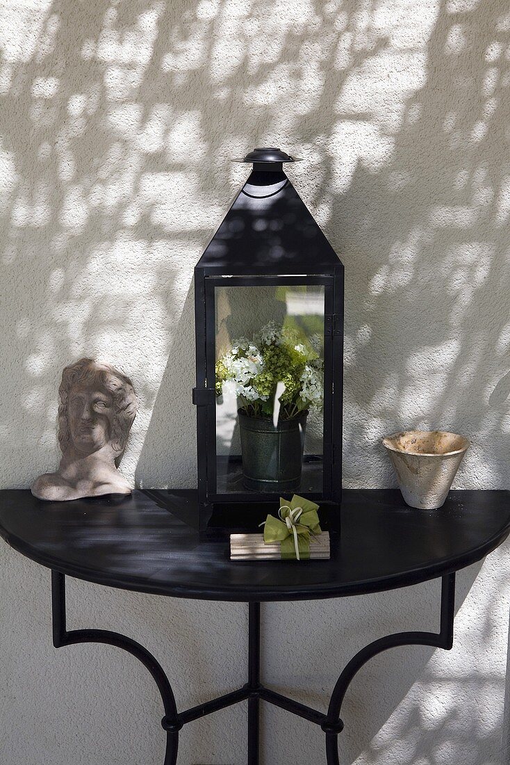 Lantern and ceramics on a black console table in front of a white house facade