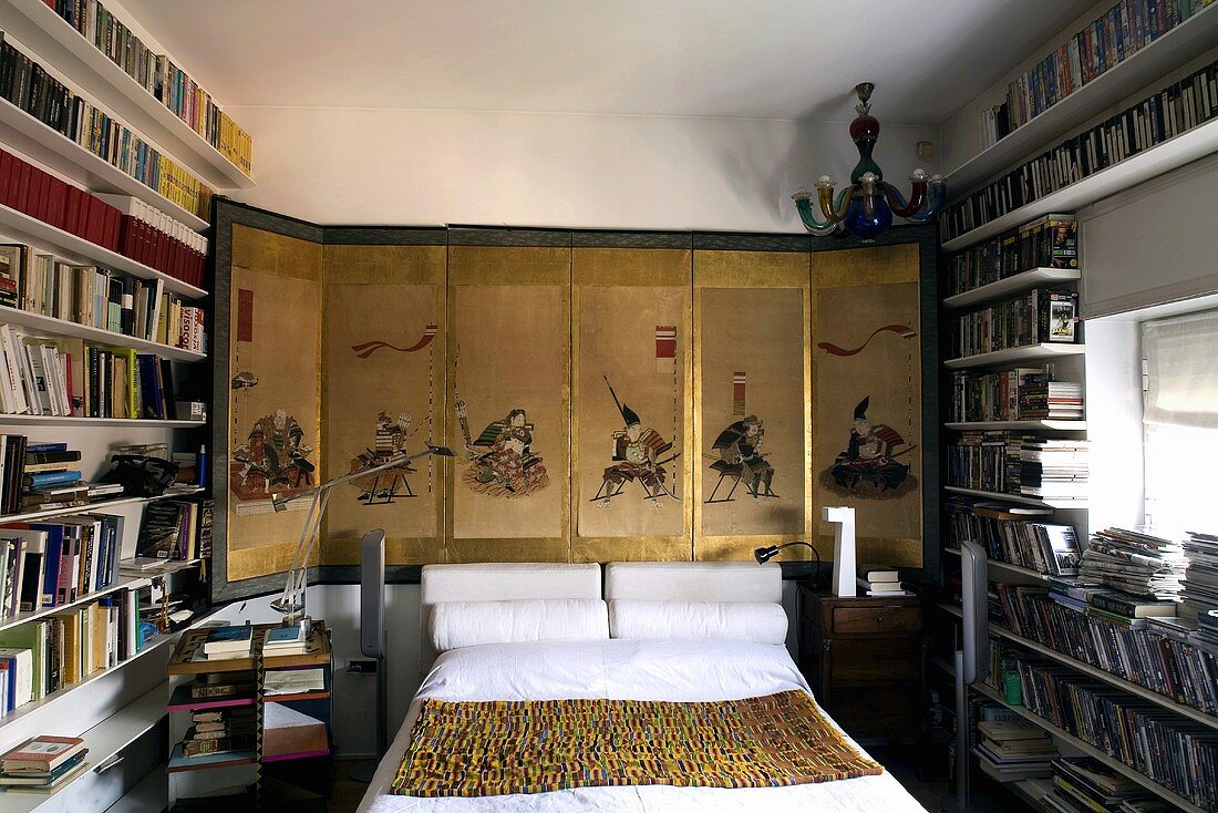 Bedroom with a double bed in front of an Asian screen and floor to ceiling bookshelves