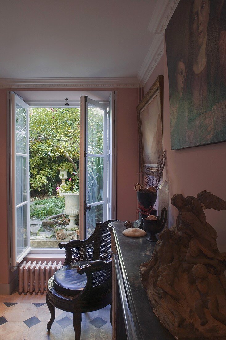 Wohnraum mit Antiquitäten und Blick durch geöffnetes Fenster in Garten