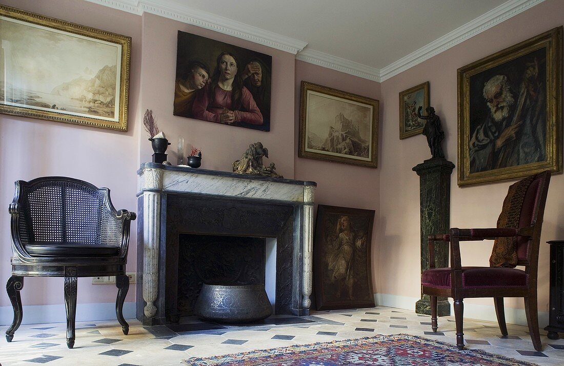 Living room in an old building with antique chairs in front of a fireplace with paintings on a pink wall