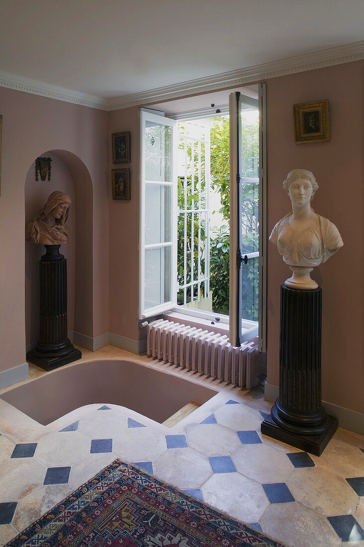 Pink anteroom with a tiled floor and busts next to a stair entrance and open window