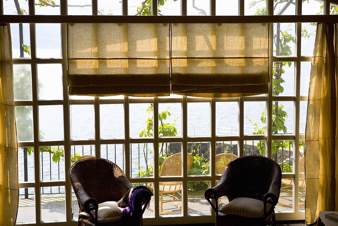 Sunny day - wicker chairs in front of lattice windows with a view of a terrace and the ocean