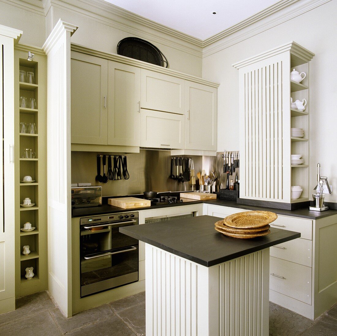 Light gray built in kitchen in elegant country house style and square island with a black work surface