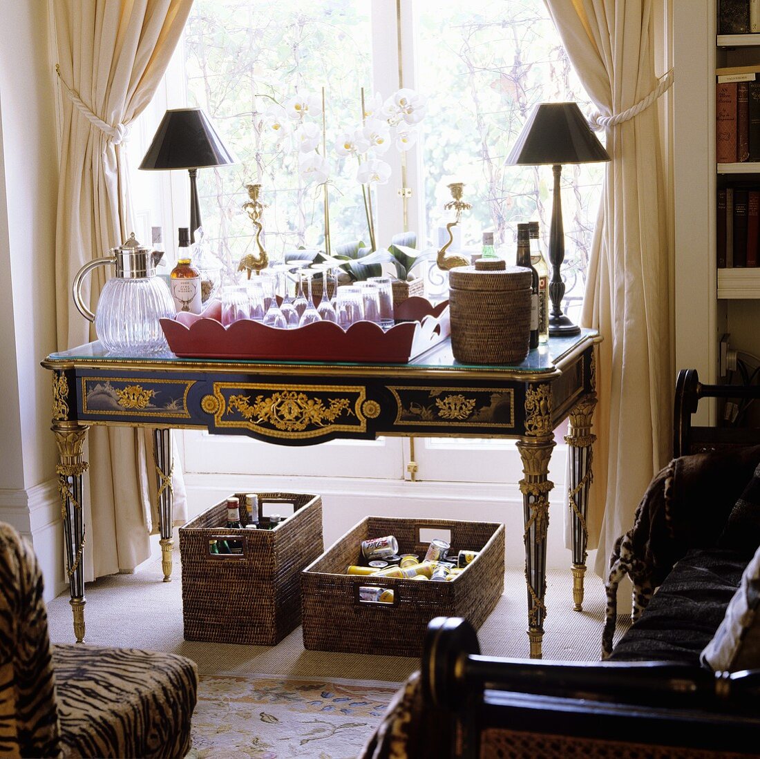 Barocker Tisch mit Gläsern auf Tablett darunter Hausbar in Körben vor raumhohem Fenster