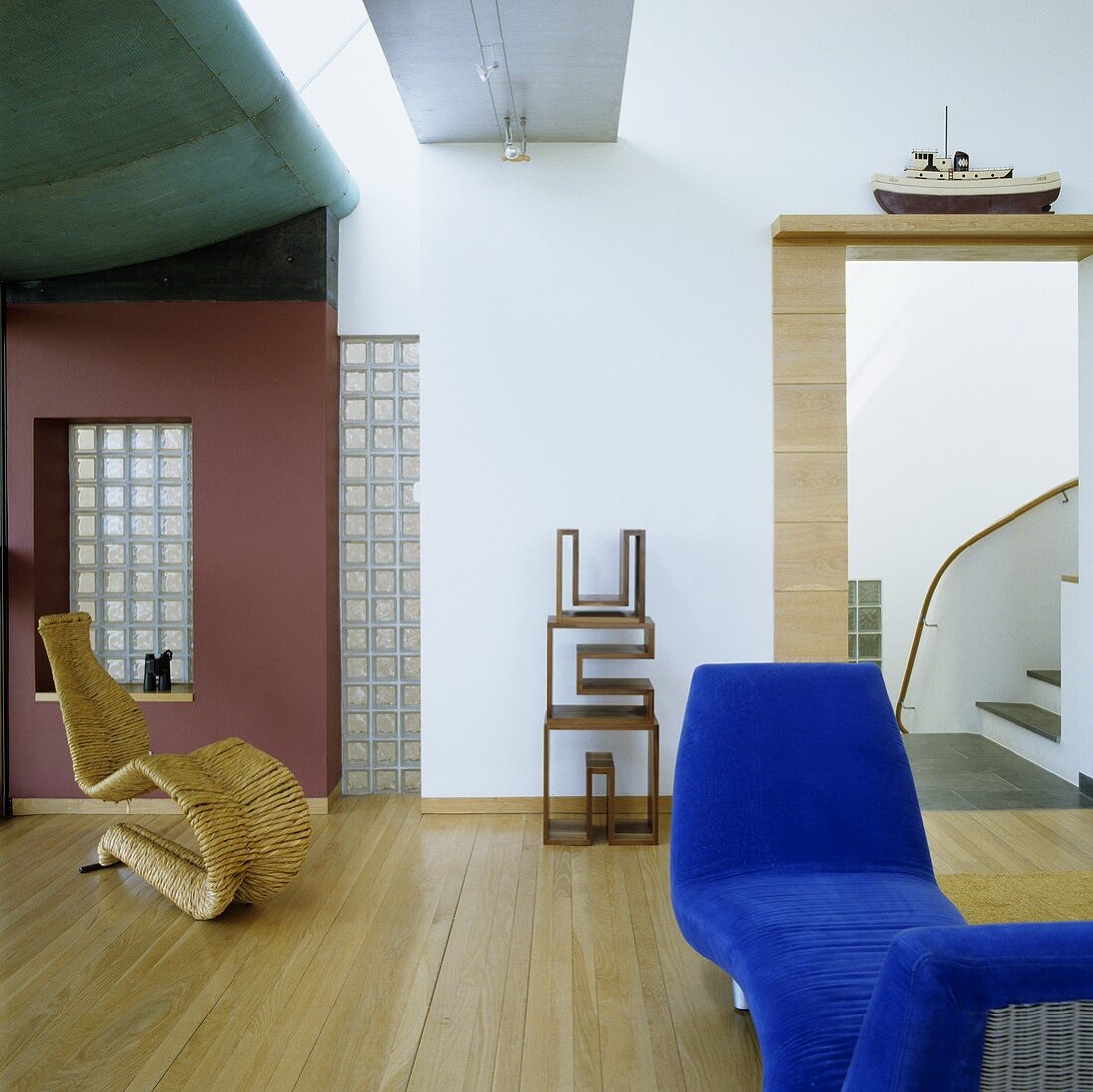Blauer Diwan und Designerstuhl aus Rattan vor roter Wand im Wohnraum
