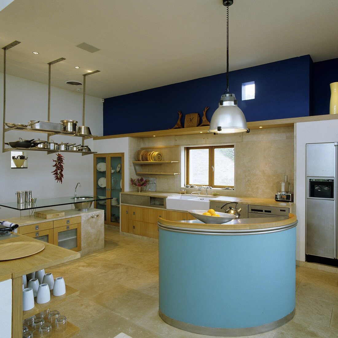 The charm of various materials - a blue-painted, round island counter with concrete kitchen furniture with wooden door in the background