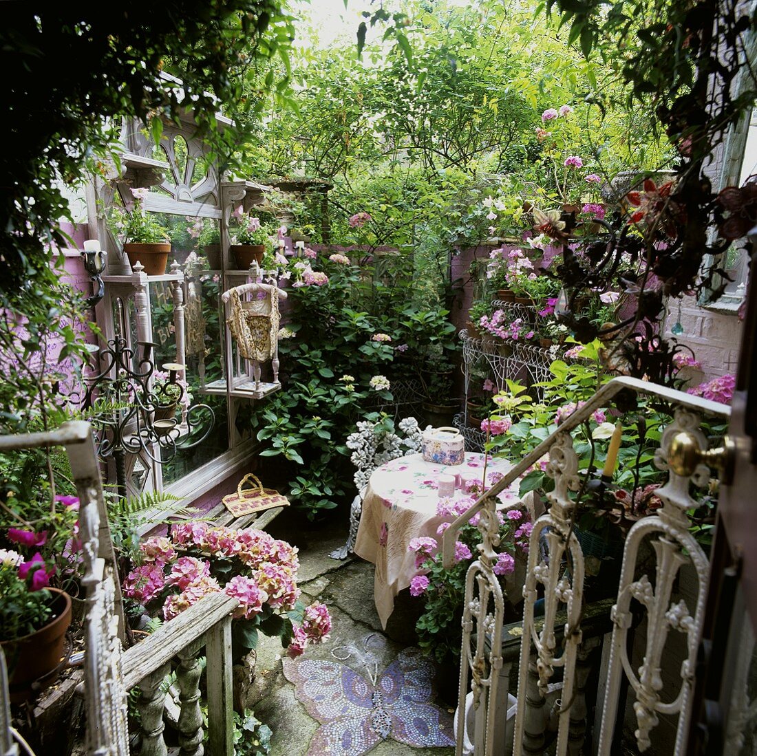 Blick auf weisses Metall Treppengeländer und romantischen Hinterhof mit Terrassentisch zwischen Grünpflanzen