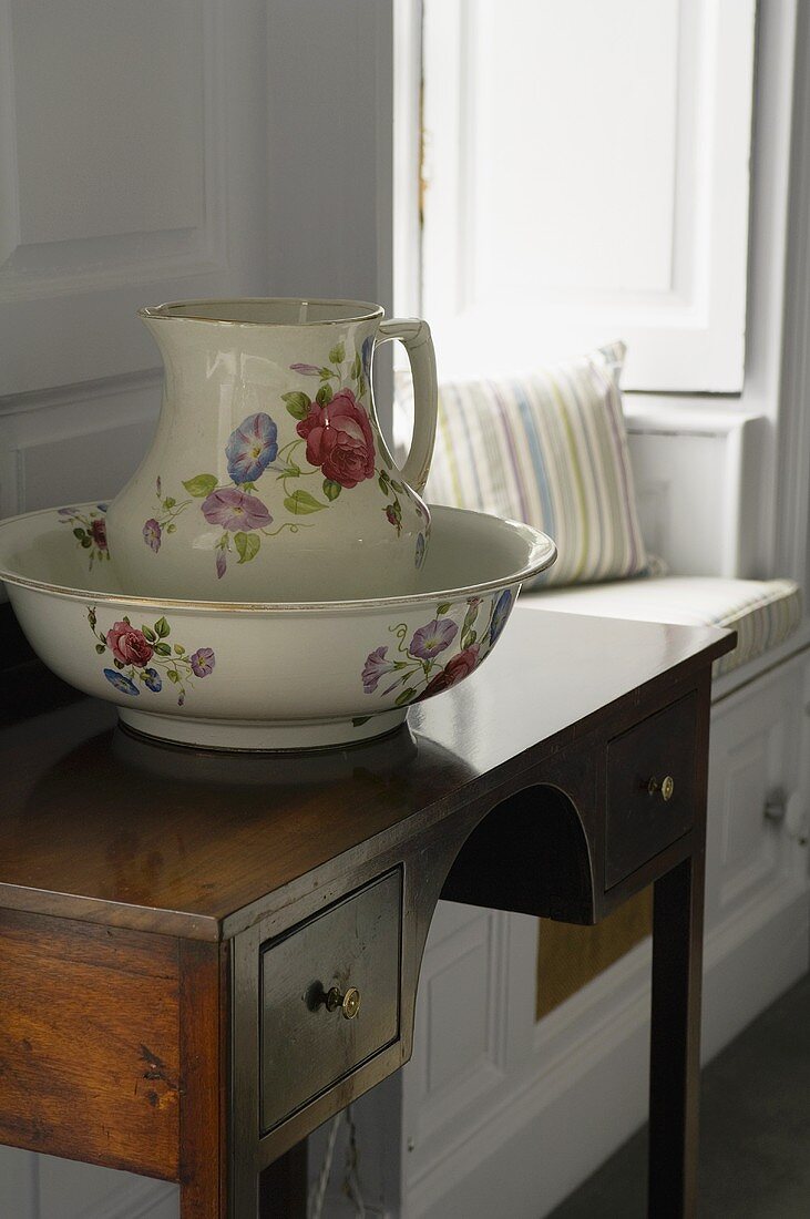 A washing bowl with a jug on a wall table with drawers