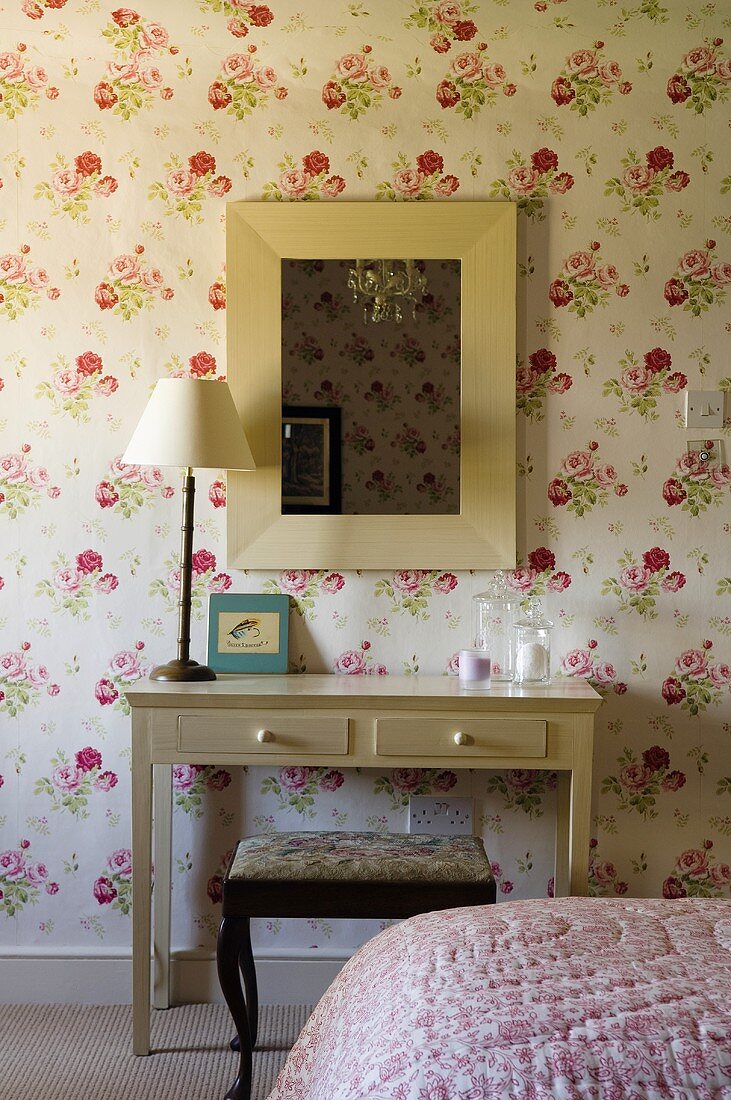 A table lamp on simple wall table standing against a floral papered wall in a bedroom